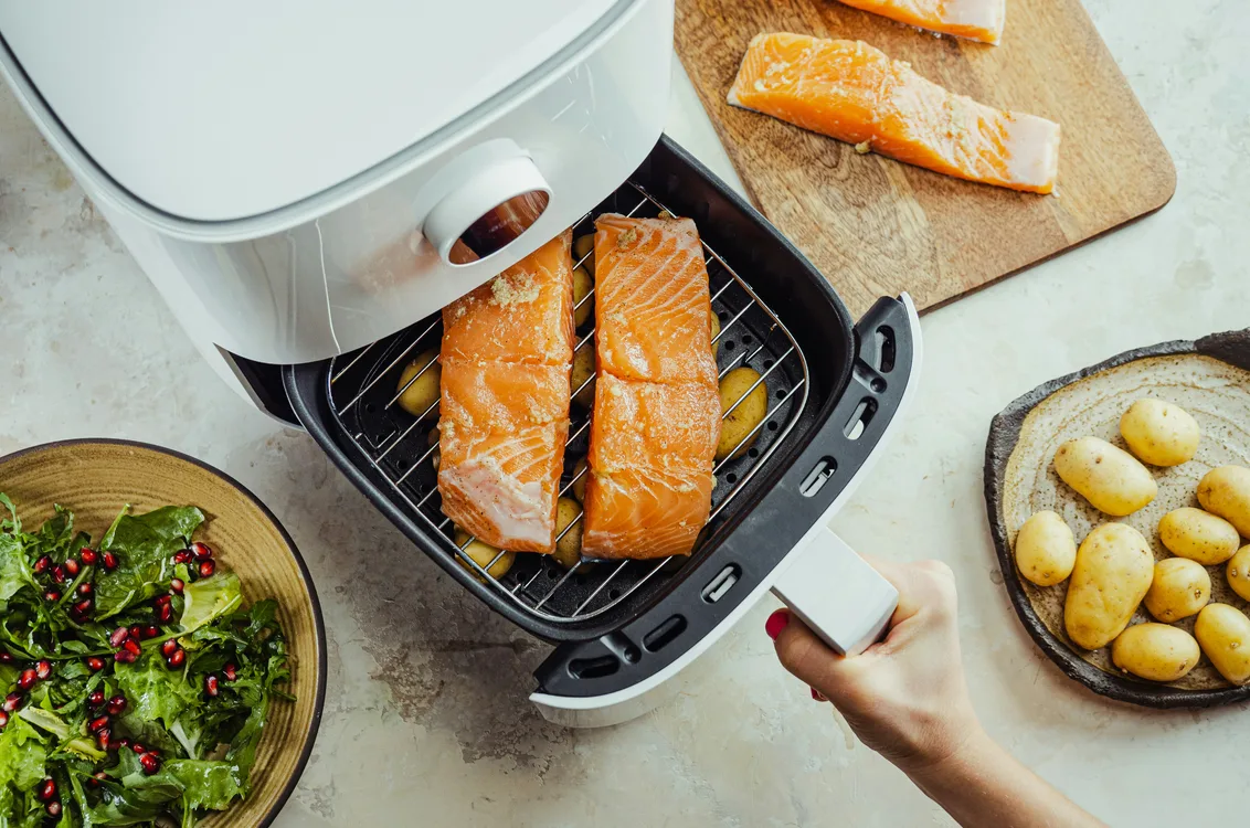 Salmon fillets on the rack of an open air fryer basket beside potatoes and salad