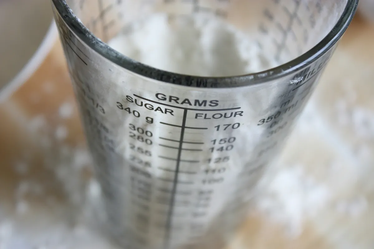 Close-up of a glass measuring cup marked in grams for sugar and flour