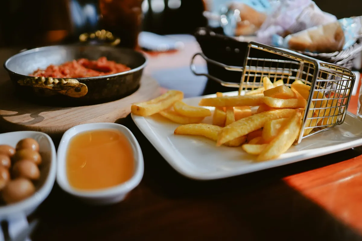 A small wire basket of golden fries tipped onto a white plate beside dips
