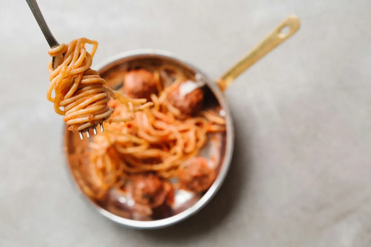 Spaghetti with meatballs twirled on a fork above a small steel pan
