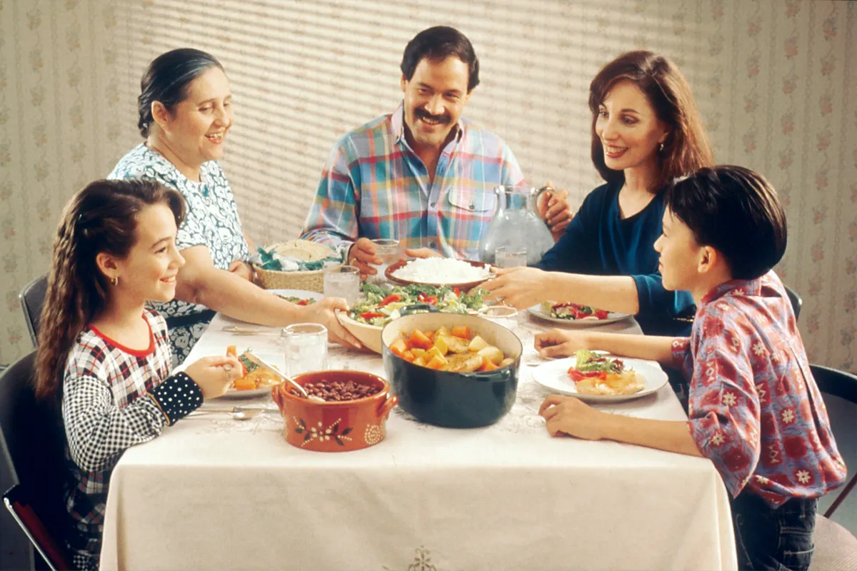 Family of five passing bowls of rice, vegetables and beans around a dinner table