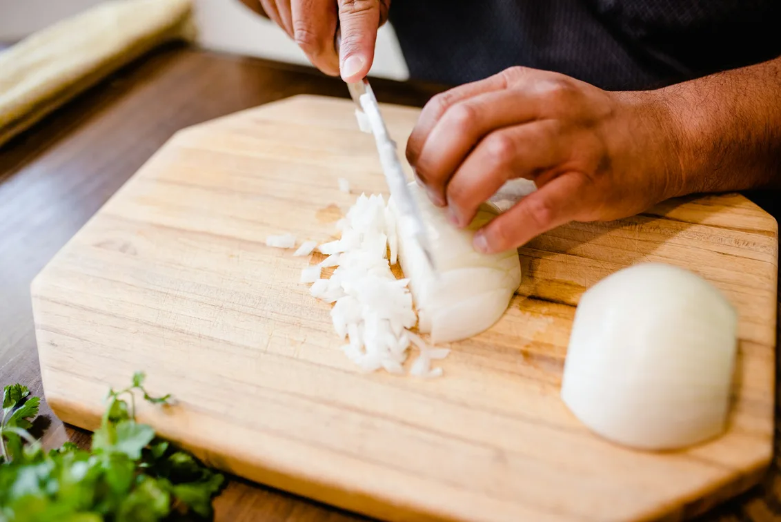 A person dicing onions with a chef's knife on a wooden cutting board