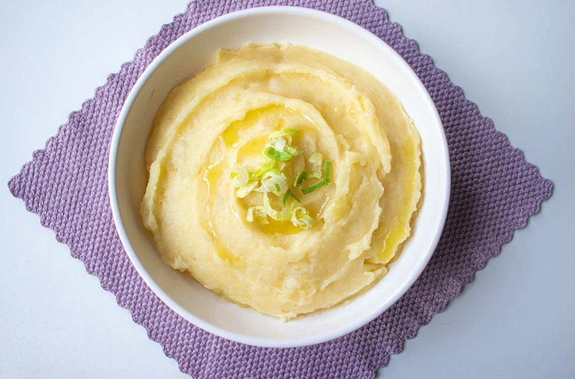 Potato ricer and masher next to a bowl of fluffy mashed potatoes