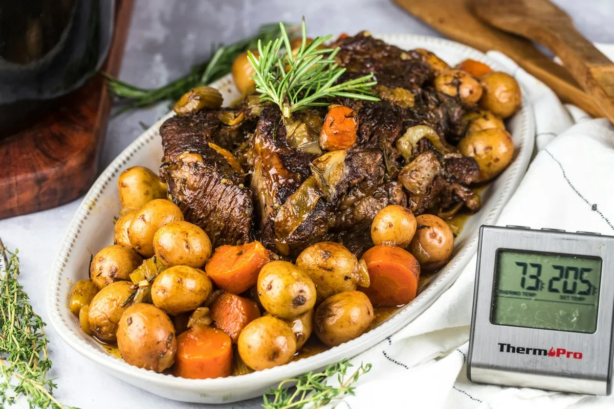 A whole chicken and vegetables cooking inside an open oval slow cooker next to an electric pressure cooker