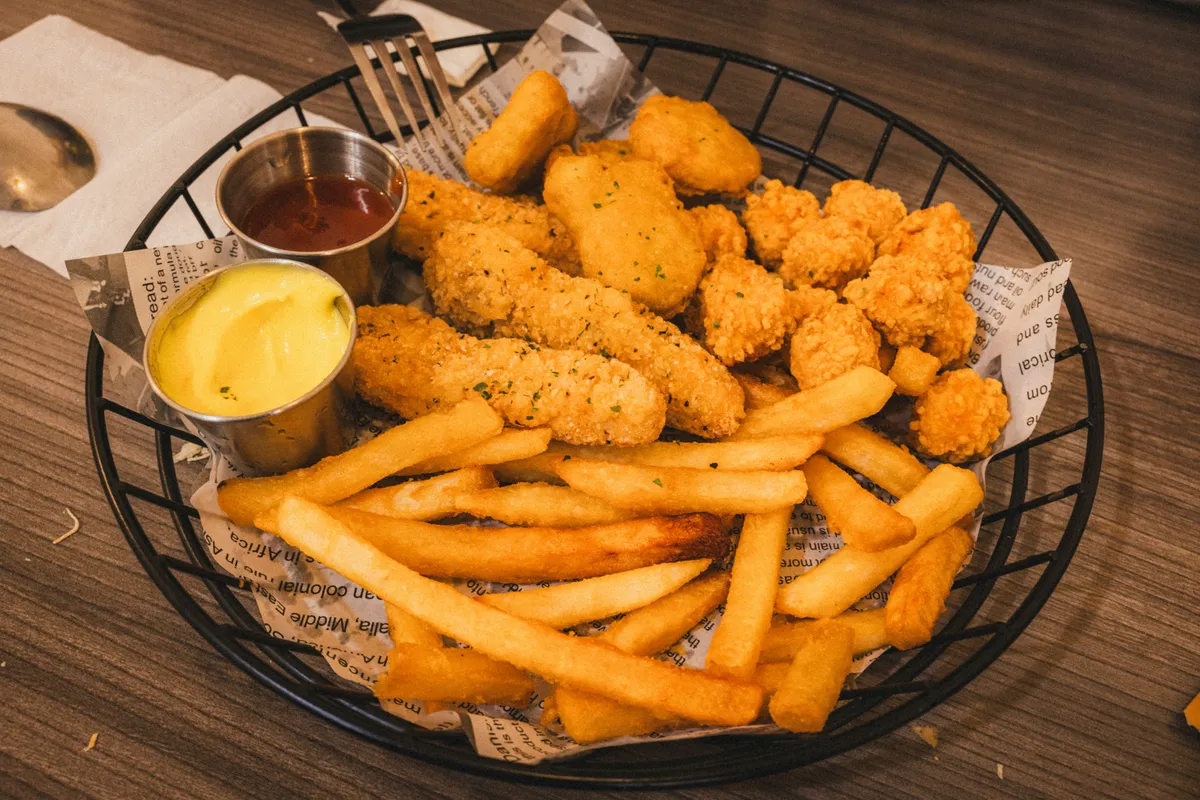 A wire basket of breaded chicken tenders and fries with two dipping sauces