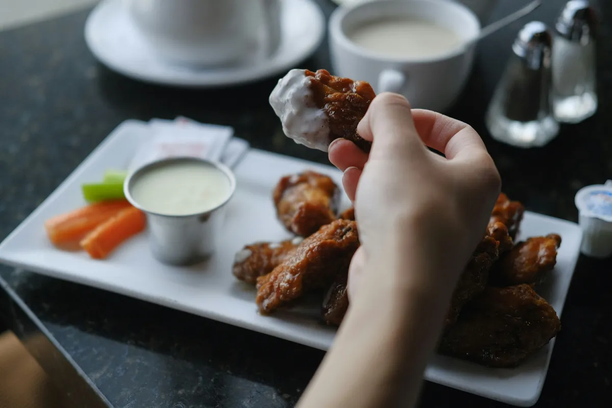 A hand dipping a wing into a bowl of cool ranch sauce
