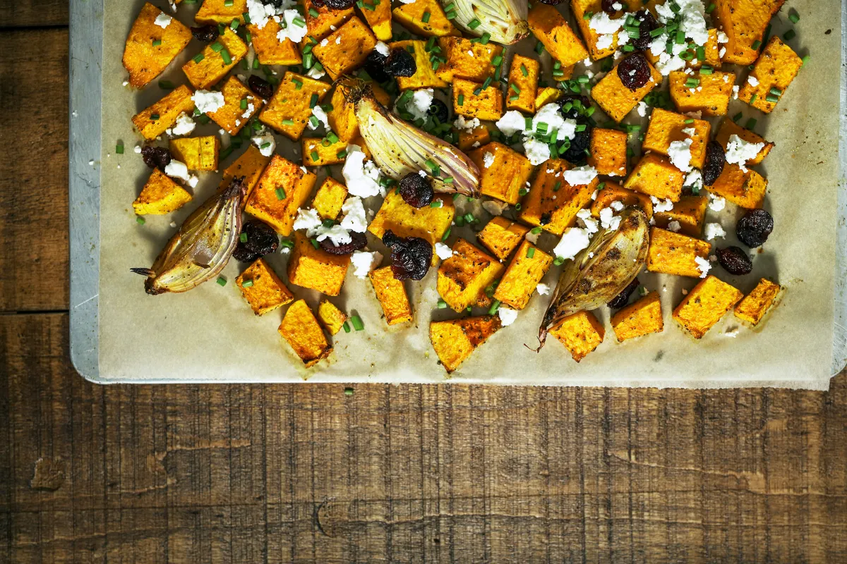 Roasted squash cubes with feta and shallots on a lined baking tray