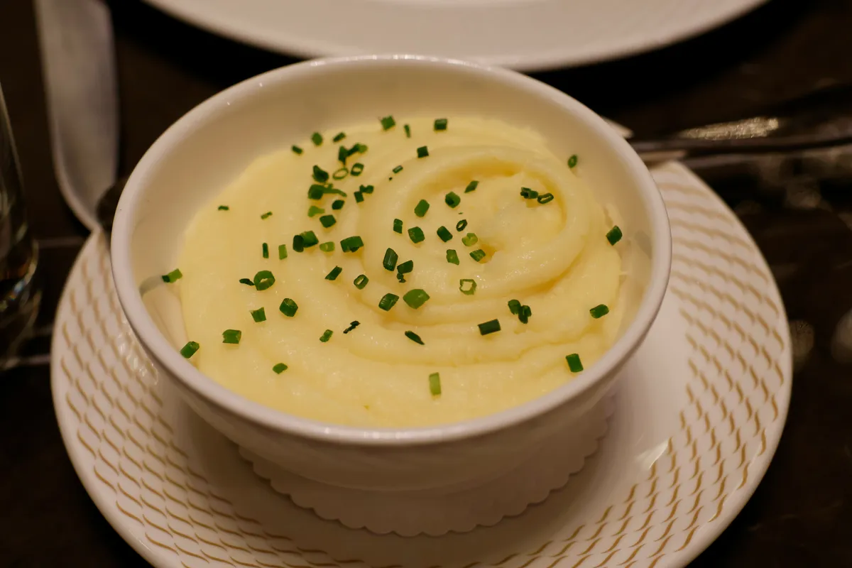 A bowl of smooth mashed potato finished with chopped chives