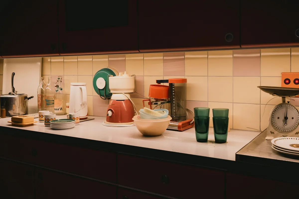 Warmly lit kitchen counter with small appliances, bowls and glasses along a tiled backsplash