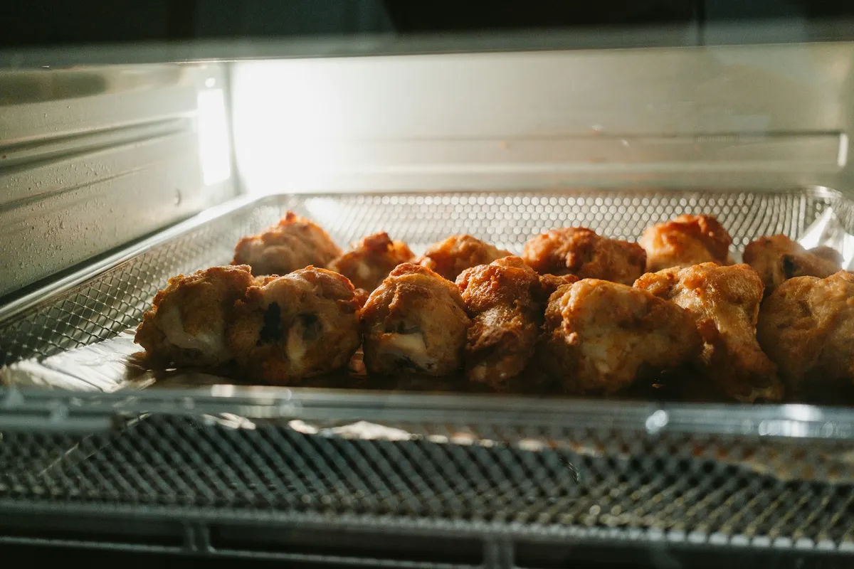 Golden fried chicken pieces resting in a mesh air fryer tray under bright light