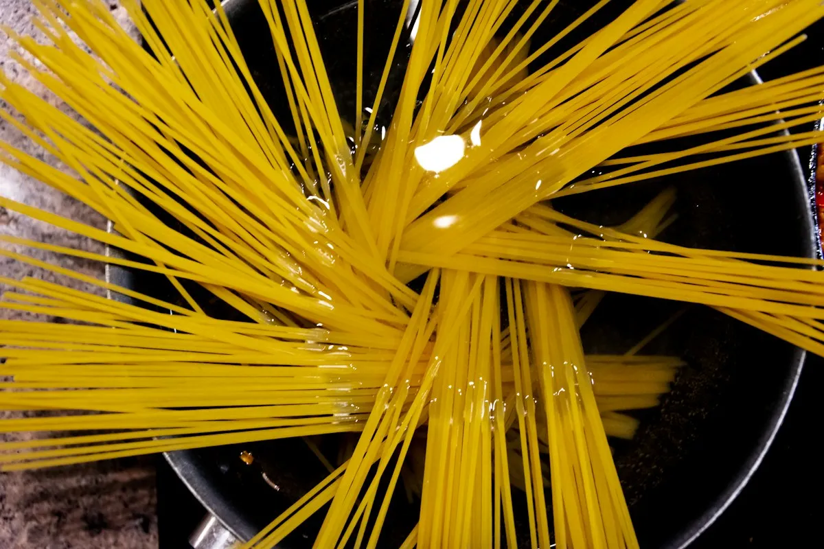 Dry spaghetti strands going into a pot of water on the stove