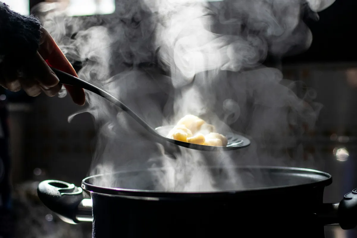 Steam rising from a dark pot as a slotted spoon lifts out cooked food