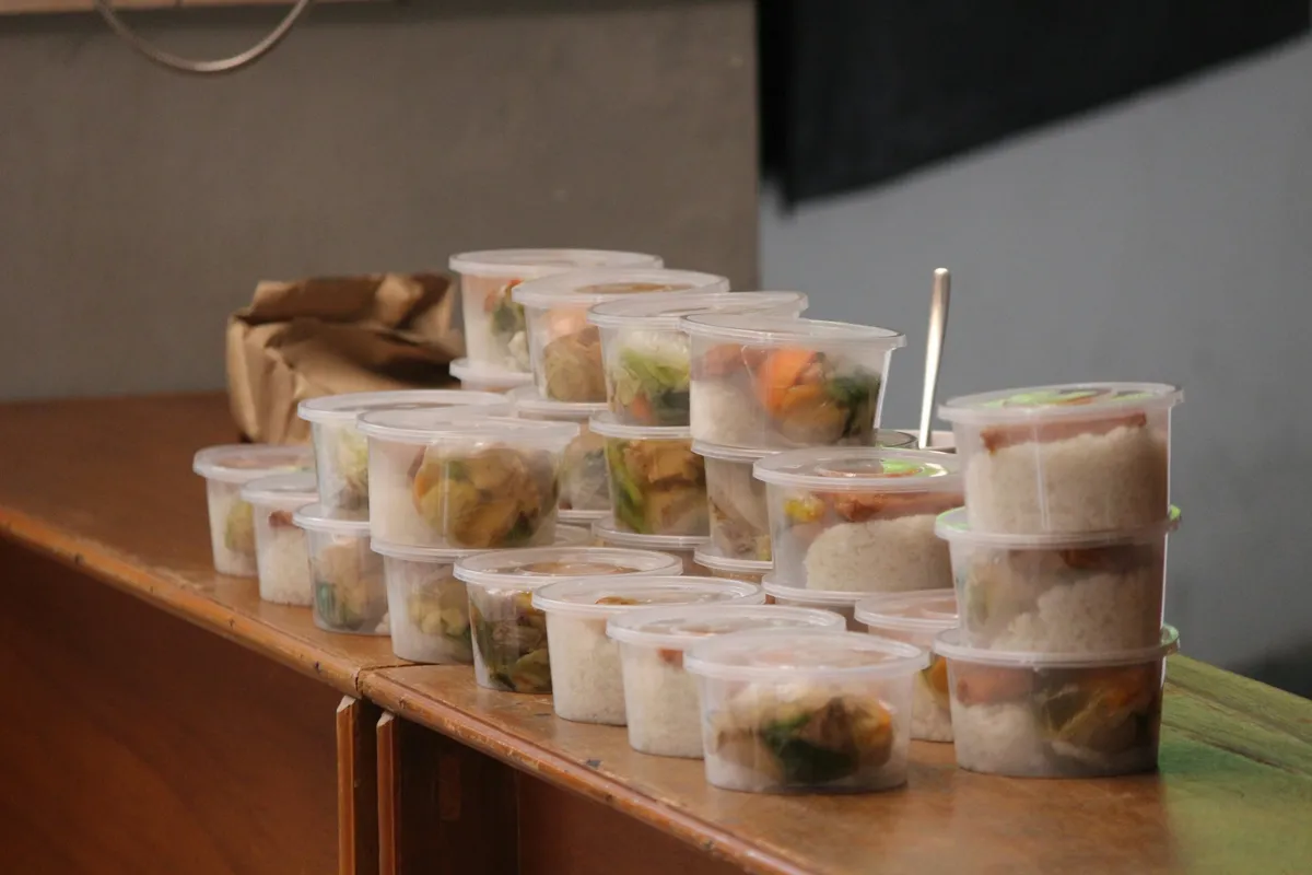 Clear lidded deli cups of rice and vegetables stacked on a wooden counter