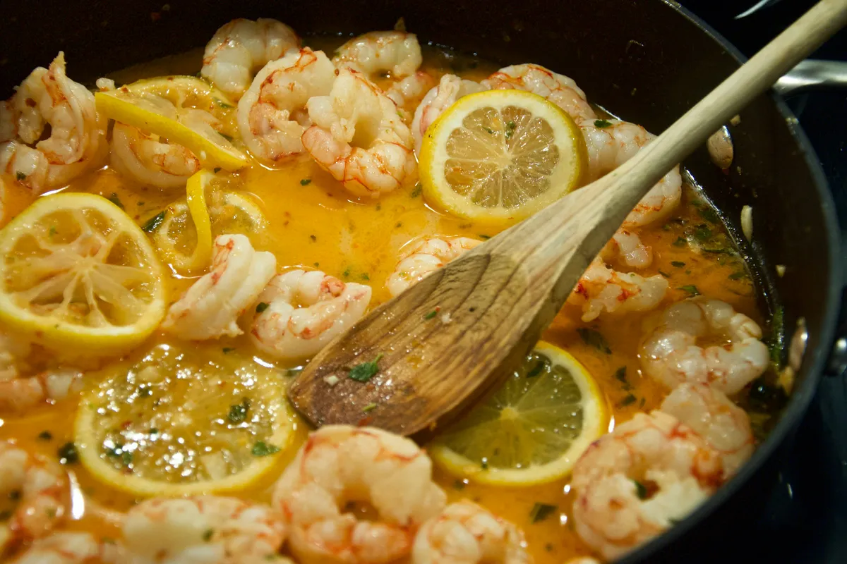 Shrimp scampi plated with lemon and a spoon of pan sauce