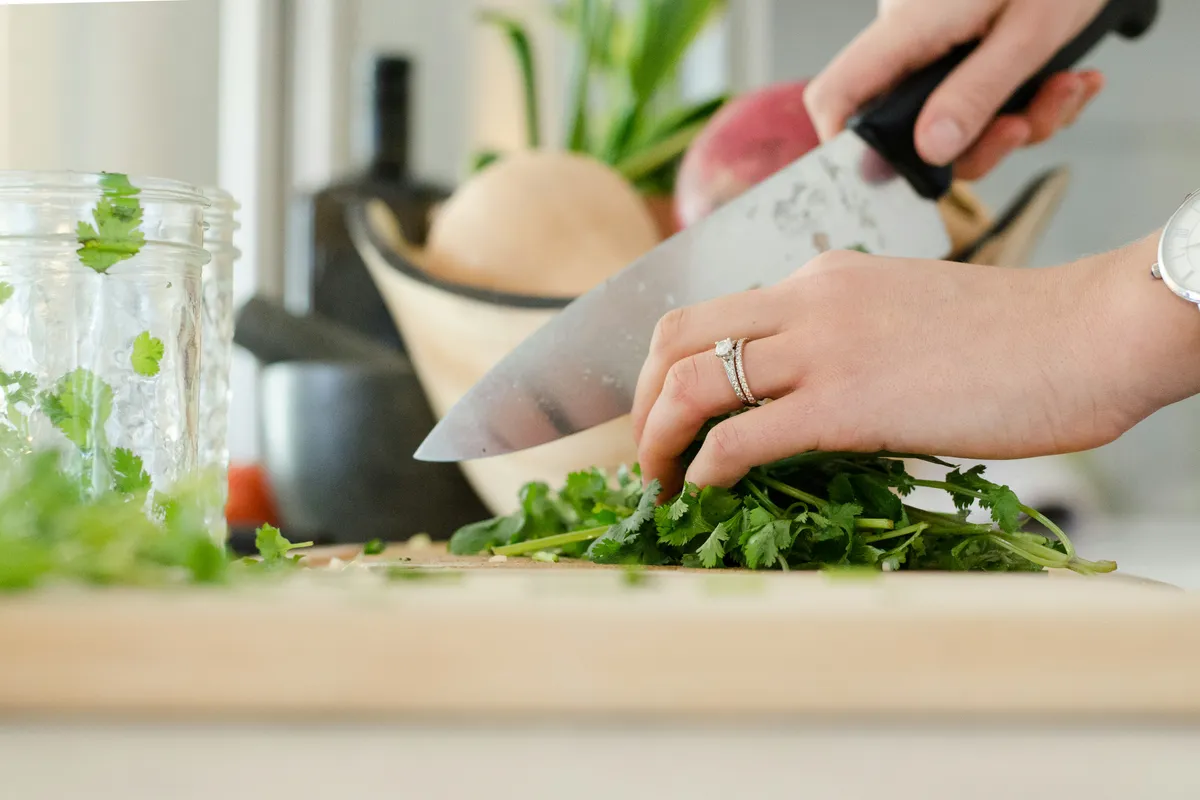 Hands using a chef knife to chop fresh herbs on a wooden board