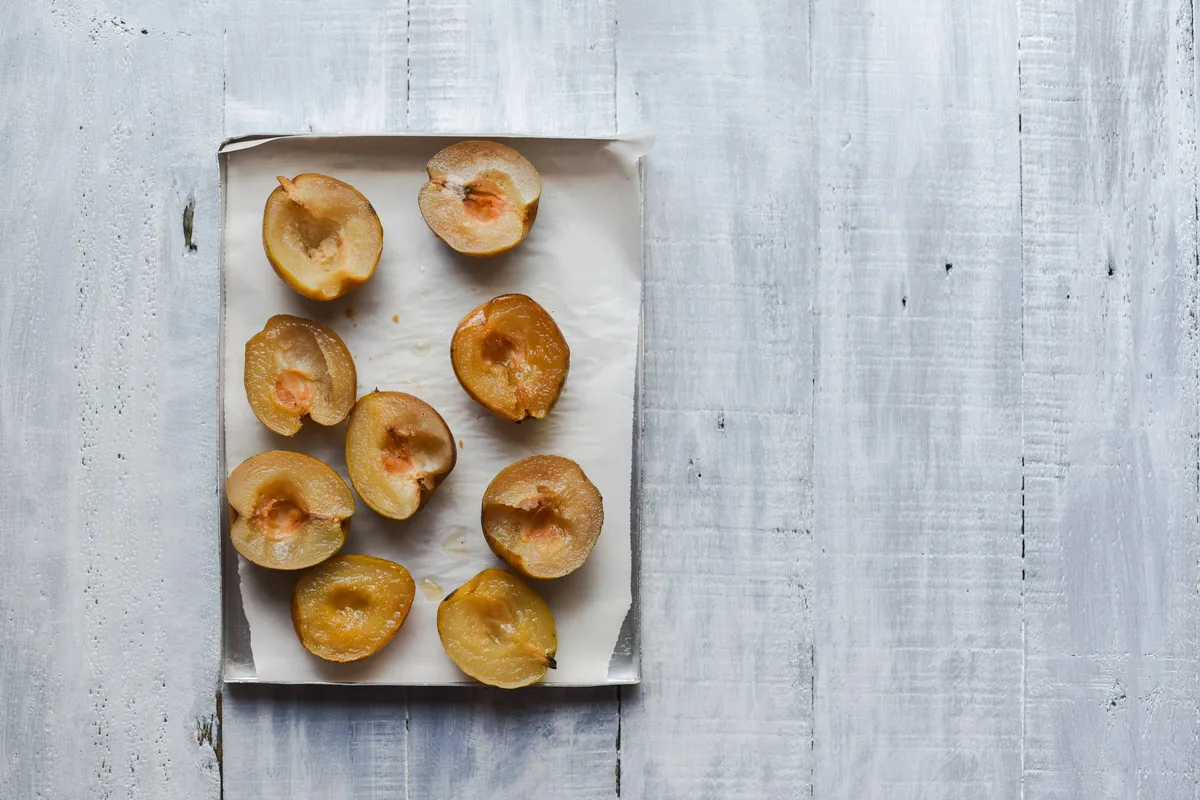 Roasted pear halves with browned cut sides on parchment over a whitewashed board