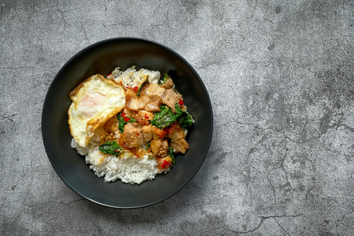 Basil pork over rice with a fried egg, served on a dark plate
