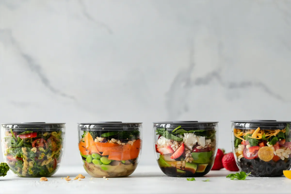 Four clear tubs of vegetables portioned out on a counter